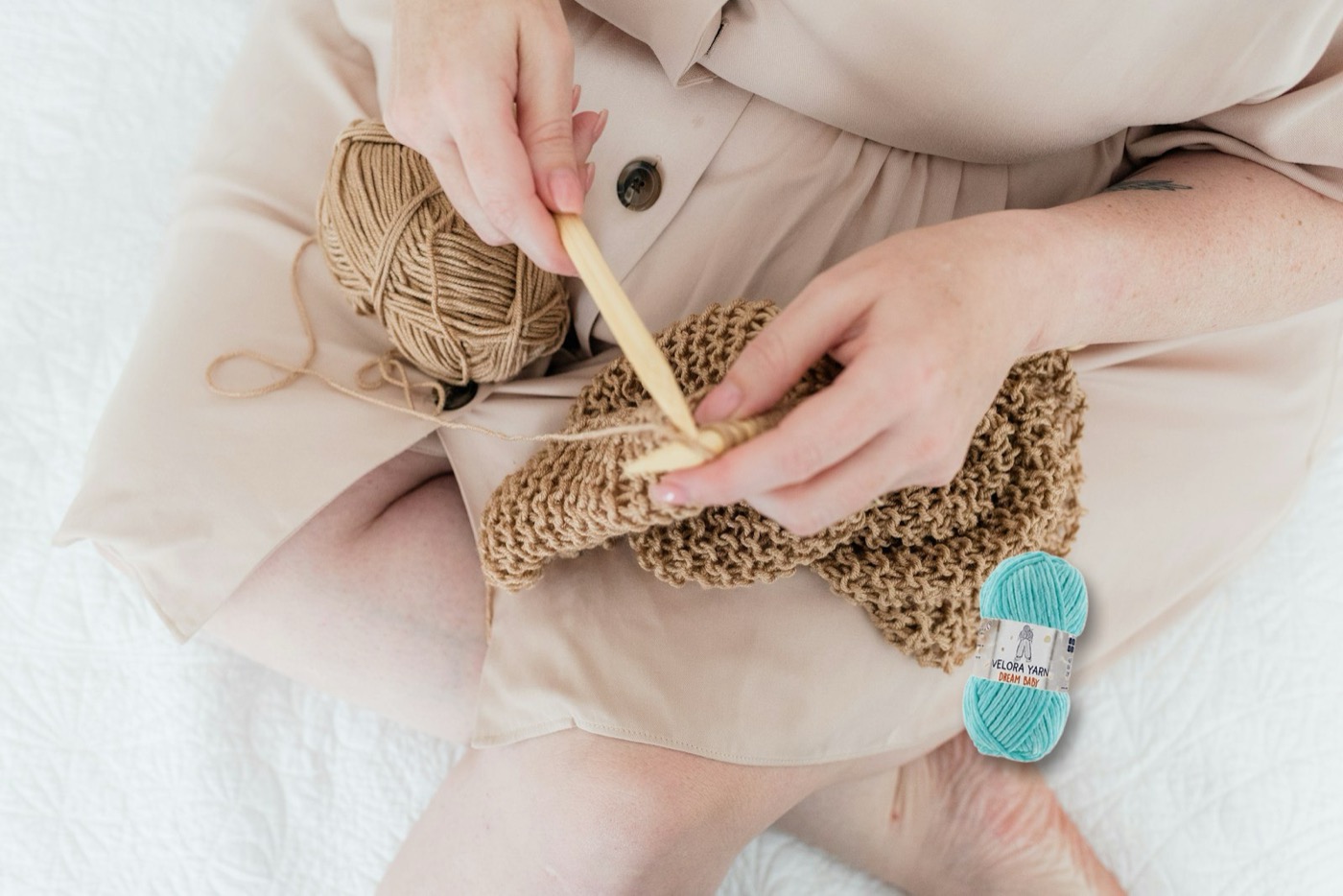 Woman crocheting with a wooden hook, a skein of Velora Dream Baby chenille yarn beside her