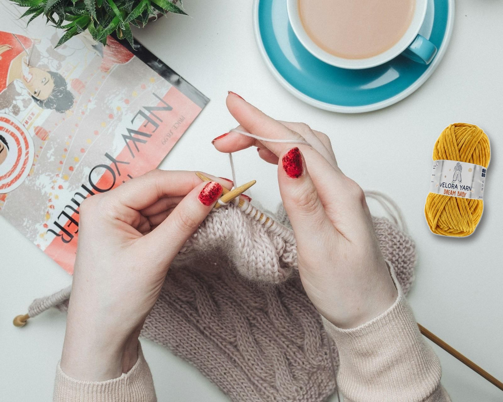 Woman knitting with Velora Dream Baby chenille yarn, cup of tea beside her